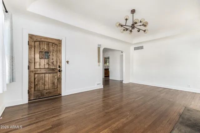 a view of an empty room with wooden floor and a chandelier