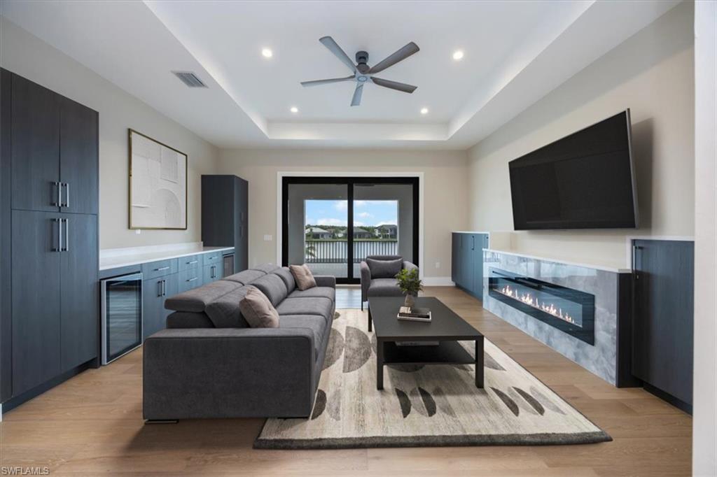 14211 Charthouse Circle Naples, FL 34114 - Photo 16 of 48 Living area with a raised ceiling, light wood-style flooring, a glass covered fireplace, beverage cooler, and a ceiling fan