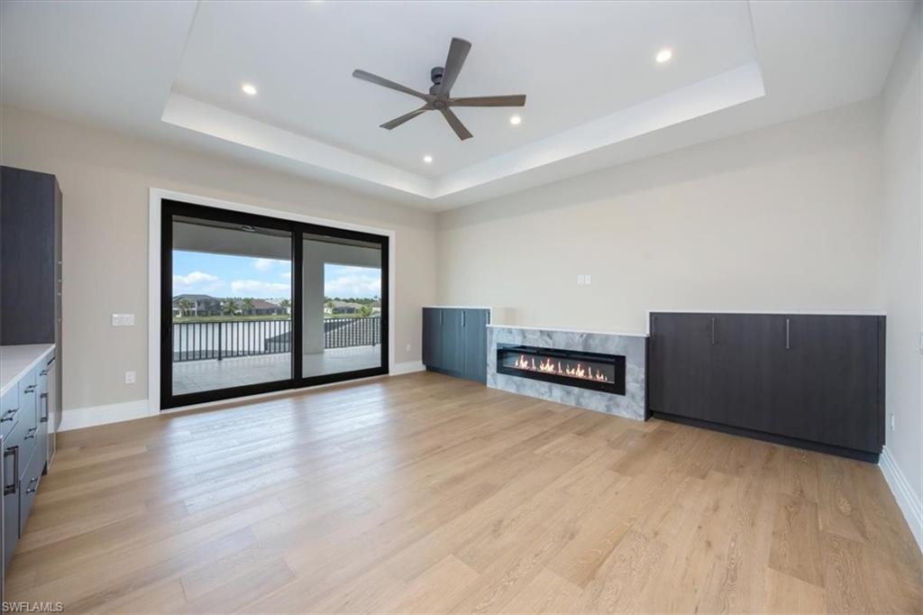 14211 Charthouse Circle Naples, FL 34114 - Photo 17 of 48 Unfurnished living room with a raised ceiling, recessed lighting, light wood-style floors, and a high end fireplace