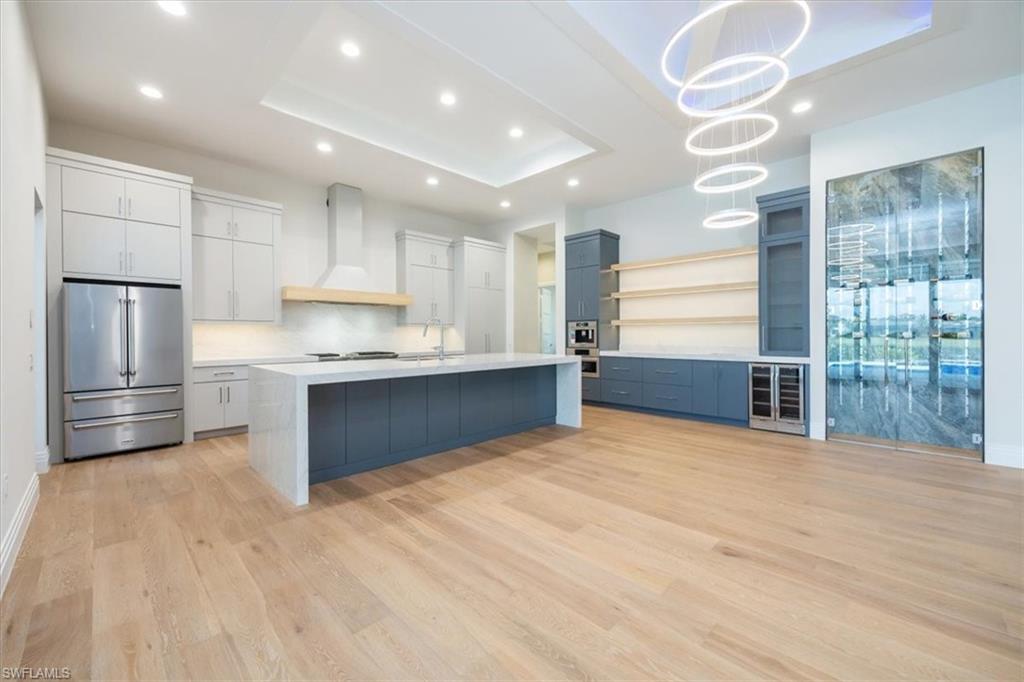 14211 Charthouse Circle Naples, FL 34114 - Photo 3 of 48 Kitchen featuring open shelves, high end fridge, a tray ceiling, light wood finished floors, and wall chimney exhaust hood
