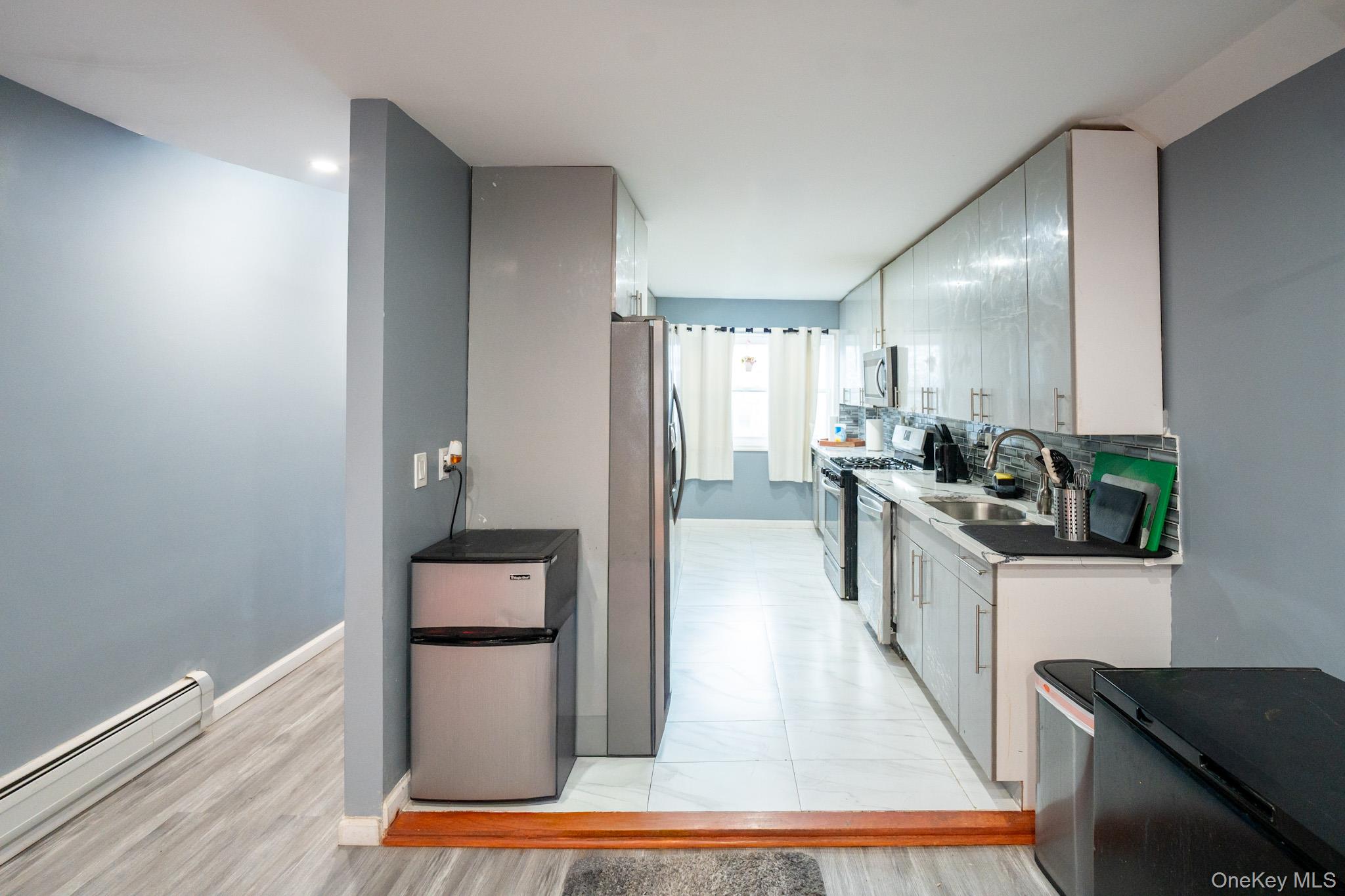 23 Yucca Drive Staten Island, NY 10312 - Photo 14 of 21 Kitchen featuring a baseboard heating unit, stainless steel appliances, tasteful backsplash, white cabinets, and light wood-style flooring
