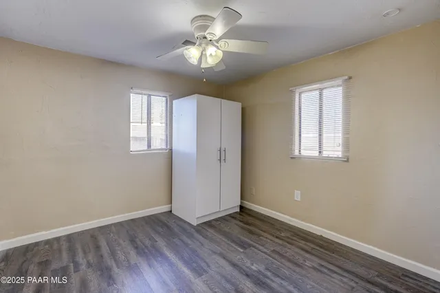 an empty room with wooden floor chandelier fan and windows