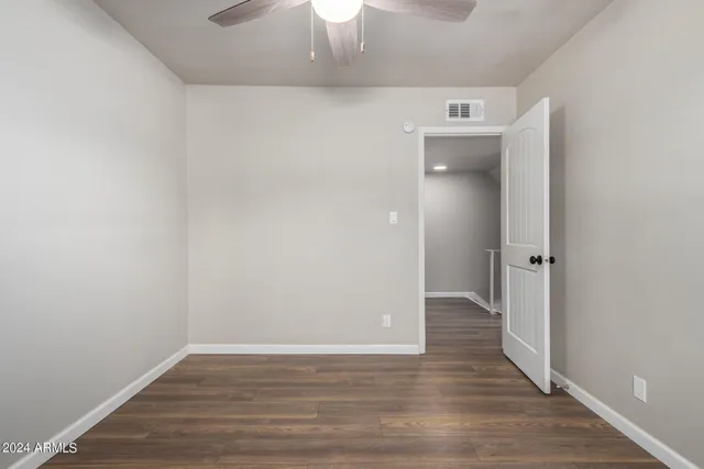 a view of an empty room with wooden floor and a ceiling fan