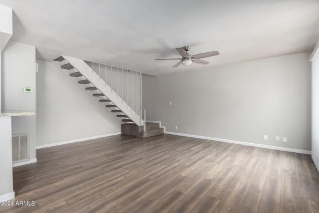 a view of an empty room with wooden floor and a ceiling fan