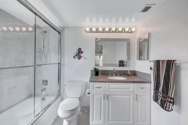 a bathroom with a granite countertop sink a toilet a mirror and shower