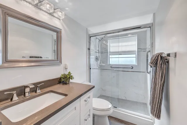 a bathroom with a granite countertop sink toilet a mirror and shower