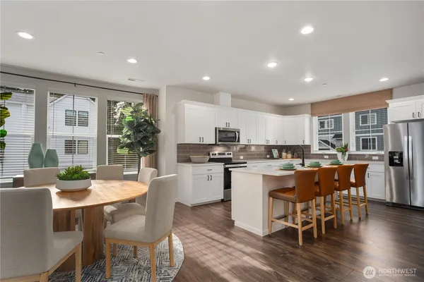 a kitchen with a dining table chairs cabinets wooden floor and appliances