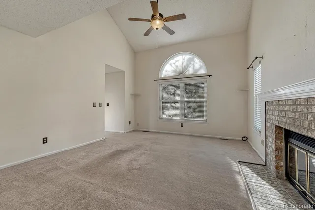 an empty room with windows fireplace and chandelier fan