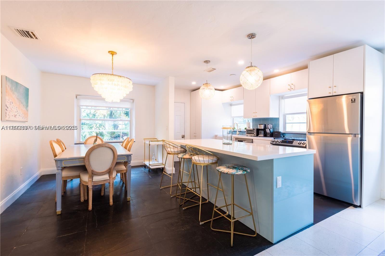 426 Northeast 26th Street, Unit 1 Miami, FL 33137 - Photo 4 of 23 a kitchen with stainless steel appliances kitchen island granite countertop a dining table chairs and a refrigerator
