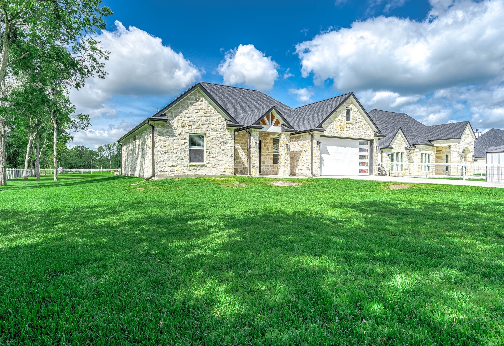8032 Short Road Needville, TX 77461 - Photo 49 of 50 This beautiful stone home features a clean modern design complemented by an expansive green lawn and scenic tree-lined surroundings. The setting offers a peaceful atmosphere while showcasing the home’s strong curb appeal and spacious outdoor environment.