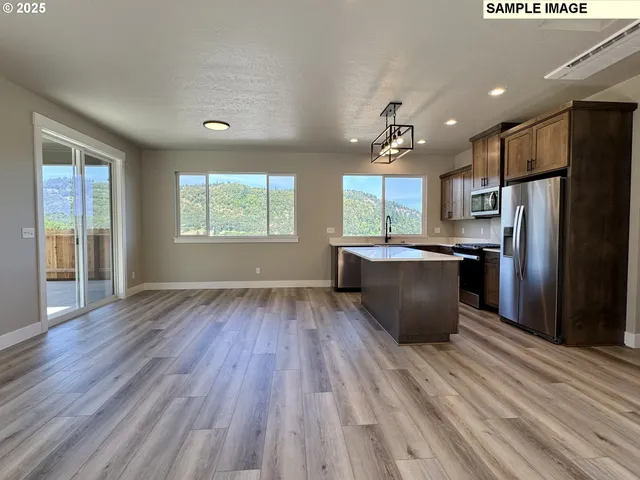 a kitchen with stainless steel appliances granite countertop a refrigerator a sink dishwasher a stove and white countertops with wooden floor