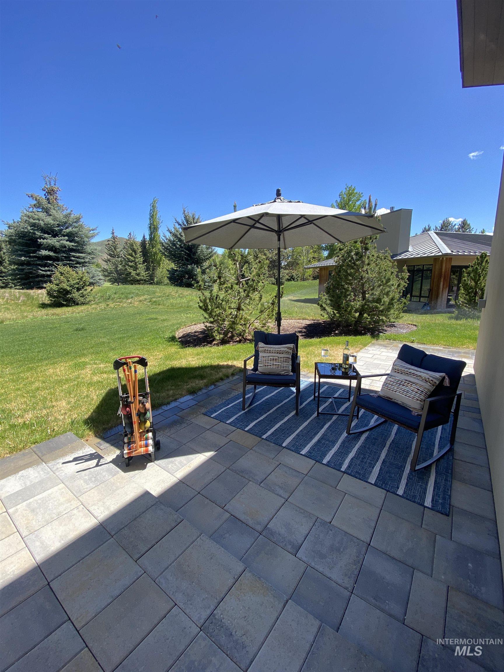 27 Streamside Drive Hailey, ID 83333 - Photo 25 of 39 Expansive paver patio with a bordering stone edge, surrounded by mature trees and a manicured lawn