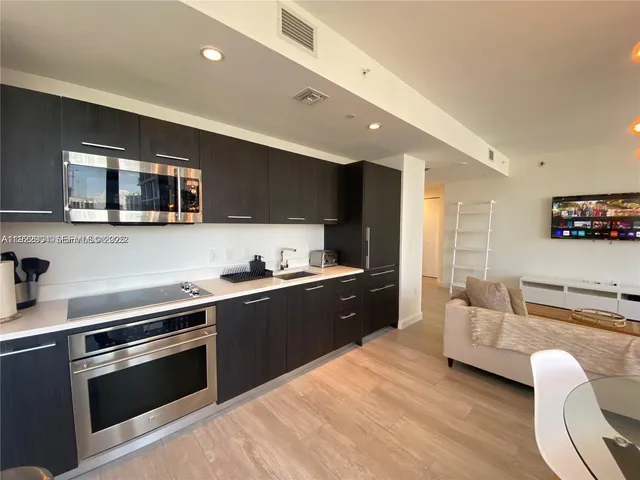 a kitchen with stainless steel appliances granite countertop a stove top oven a sink dishwasher a dining table and chairs with wooden floor