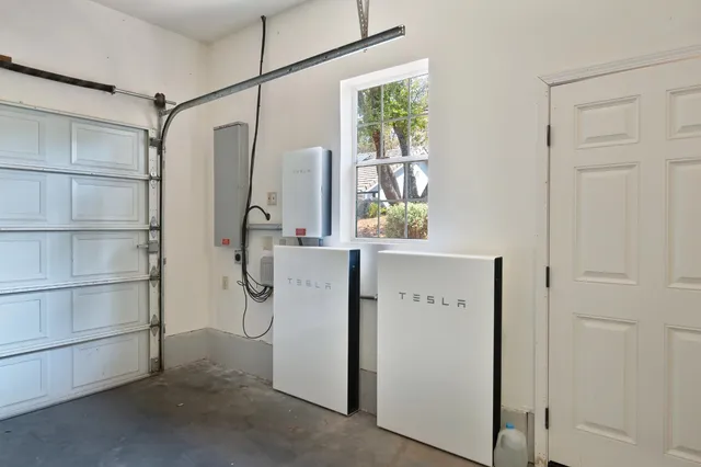 a view of a white house with large trees and wooden fence