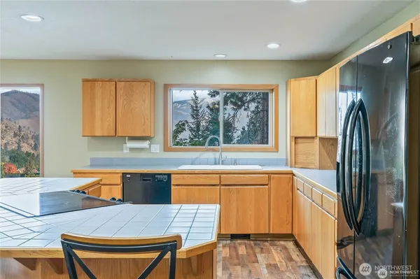 a kitchen with stainless steel appliances granite countertop a refrigerator a sink dishwasher a stove and a dining table with wooden floor