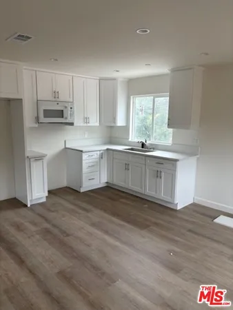 a kitchen with stainless steel appliances granite countertop a stove top oven a sink and white cabinets with wooden floor
