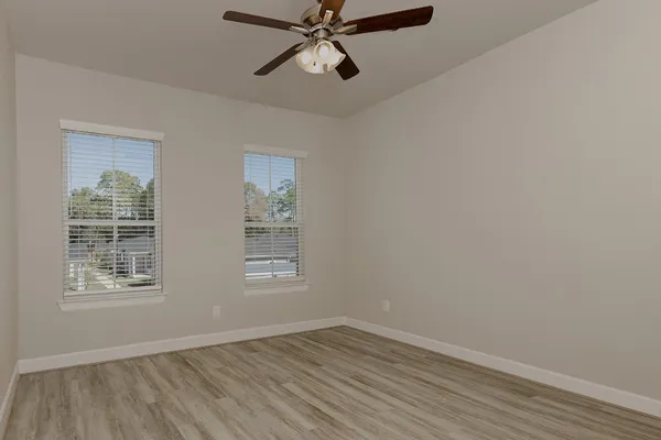 an empty room with wooden floor fan and windows