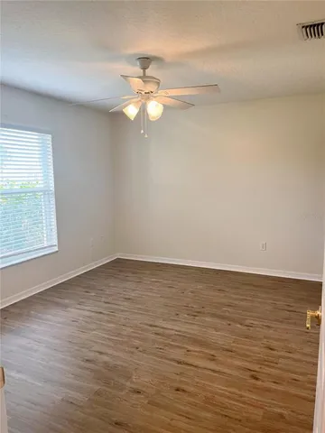 a view of an empty room with wooden floor and a ceiling fan