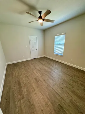 an empty room with wooden floor ceiling fan and windows