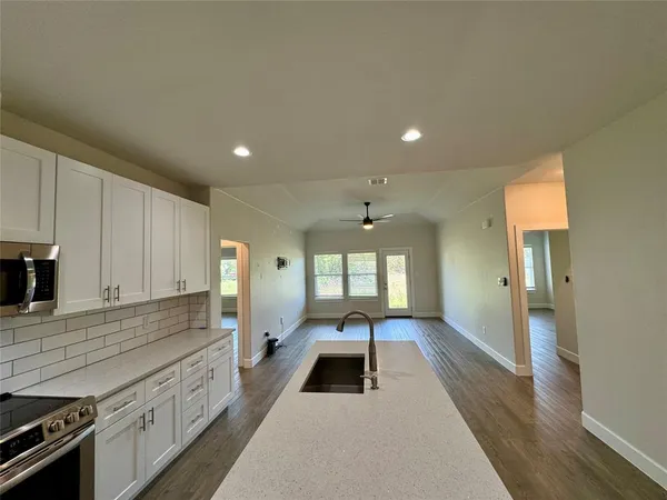 a large kitchen with granite countertop a stove a sink a refrigerator and white cabinets with wooden floor