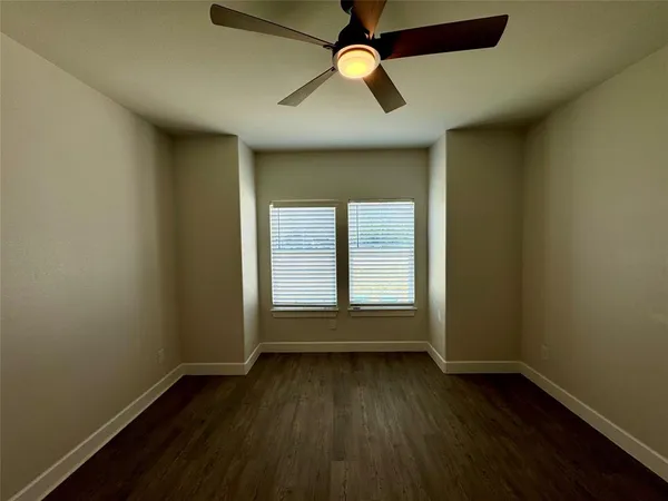 an empty room with wooden floor fan and windows