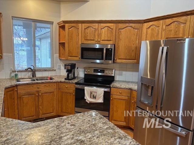 2734 North Turnberry Way Meridian, ID 83646 - Photo 2 of 18 Kitchen with appliances with stainless steel finishes, brown cabinetry, light stone counters, and decorative backsplash