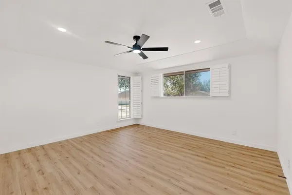 an empty room with wooden floor ceiling fan and windows