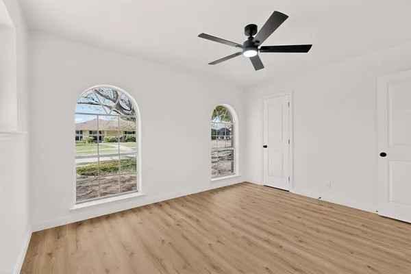 an empty room with wooden floor a ceiling fan and windows
