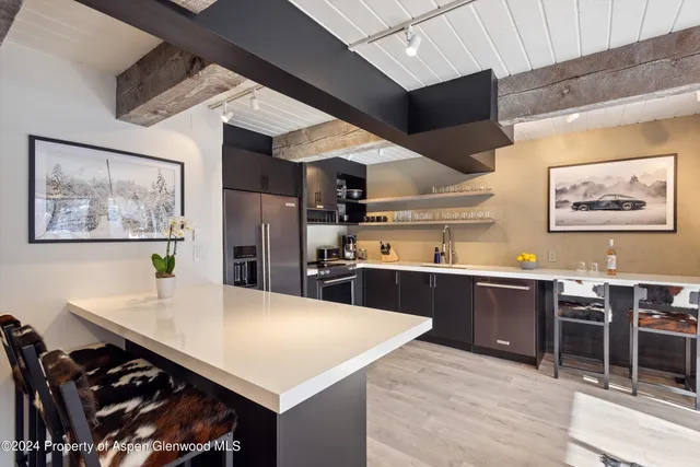 a large kitchen with stainless steel appliances a stove a refrigerator a dining table and chairs with wooden floor