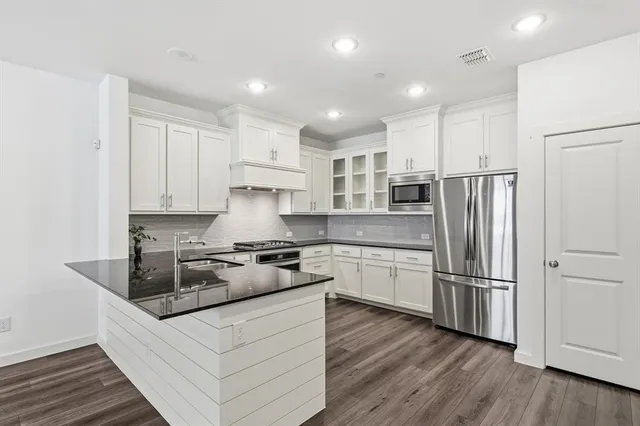 a kitchen with stainless steel appliances granite countertop a refrigerator a stove a sink and white cabinets