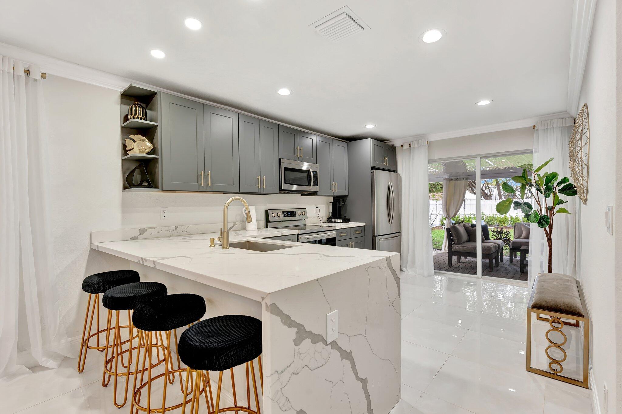 4901 Lincoln Road Delray Beach, FL 33445 - Photo 13 of 56 a kitchen with stainless steel appliances a sink a stove a refrigerator cabinets and a dining table