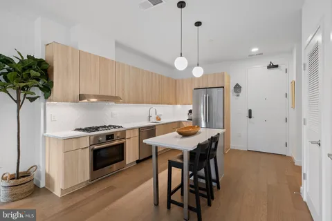 a kitchen with stainless steel appliances a stove a refrigerator a sink a dining table and chairs with wooden floor