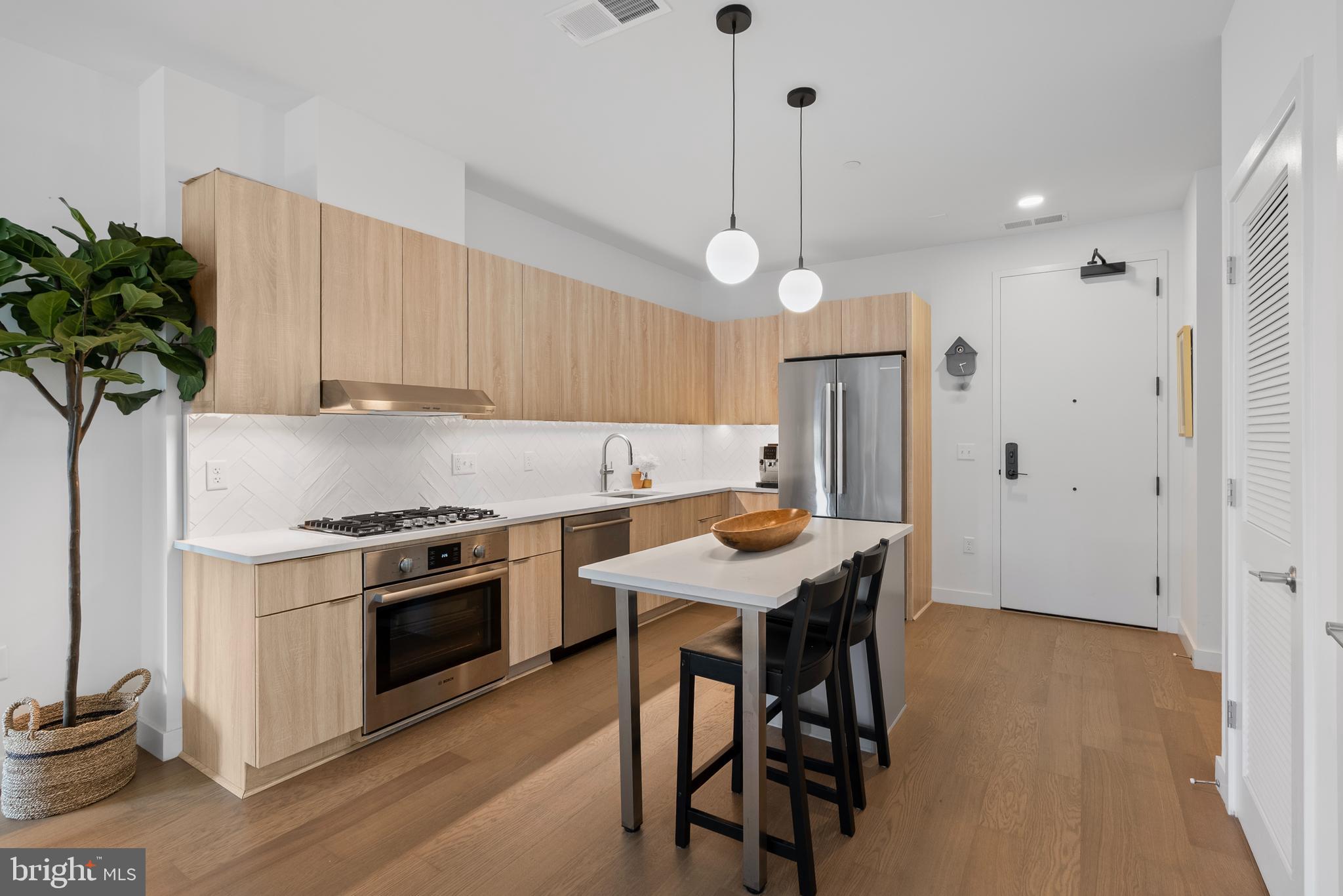 7175 12th Street Northwest, Unit 214 Washington, DC 20012 - Photo 7 of 49 a kitchen with stainless steel appliances a stove a refrigerator a sink a dining table and chairs with wooden floor