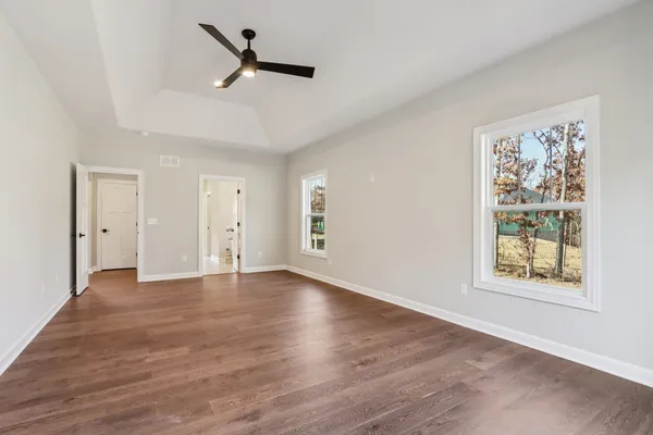 an empty room with wooden floor ceiling fan and windows