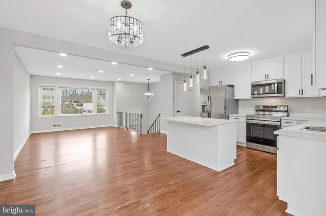 a kitchen with stainless steel appliances granite countertop a stove top oven a sink a refrigerator and white cabinets with wooden floor