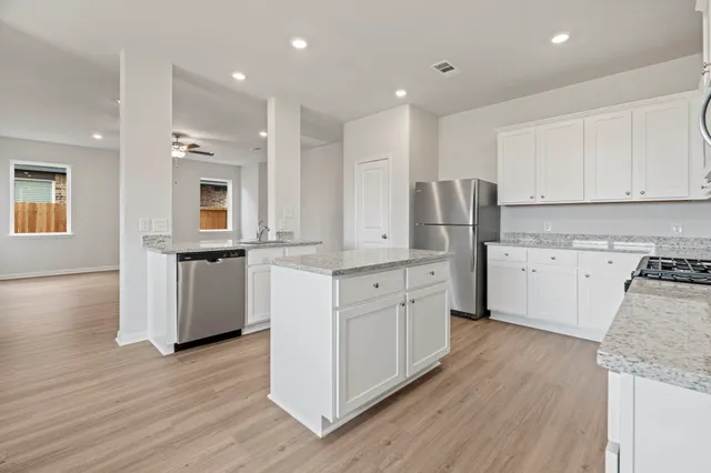 a kitchen with stainless steel appliances granite countertop a stove a sink dishwasher and a refrigerator with wooden floor