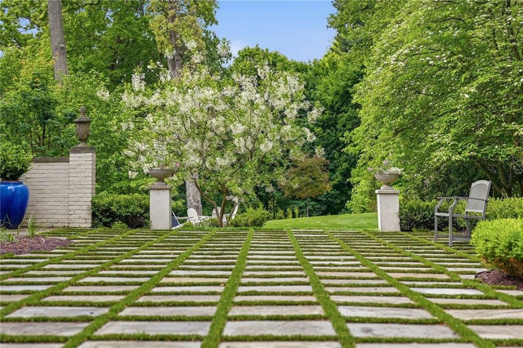 810 Persimmon Road Sewickley, PA 15143 - Photo 45 of 49 The expansive bluestone courtyard with grass-joint grid, garden bench, and deep wooded backdrop reflects the formal yet inviting character of the property's exceptional outdoor spaces.