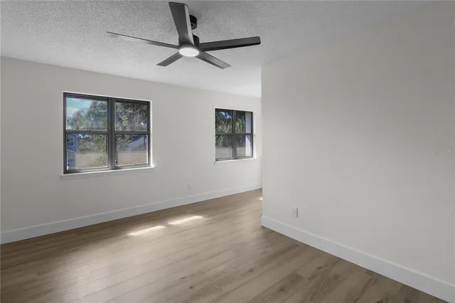 an empty room with wooden floor ceiling fan and windows