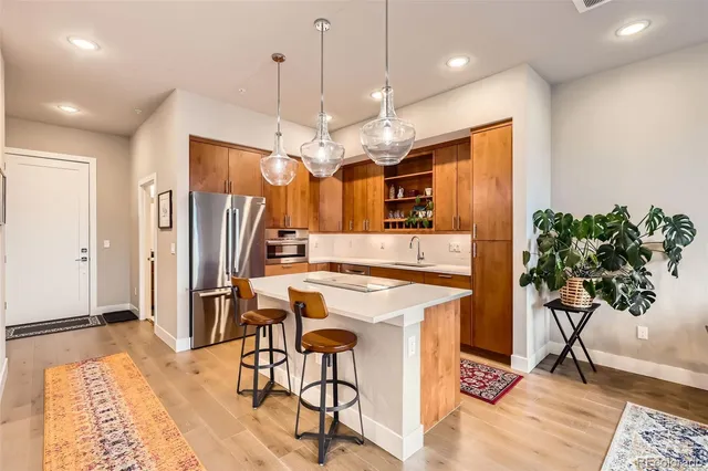 a kitchen with stainless steel appliances kitchen island granite countertop a refrigerator a oven a sink a dining table and chairs with wooden floor