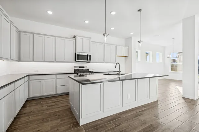 a kitchen with stainless steel appliances granite countertop a sink a stove a refrigerator and white cabinets with wooden floor