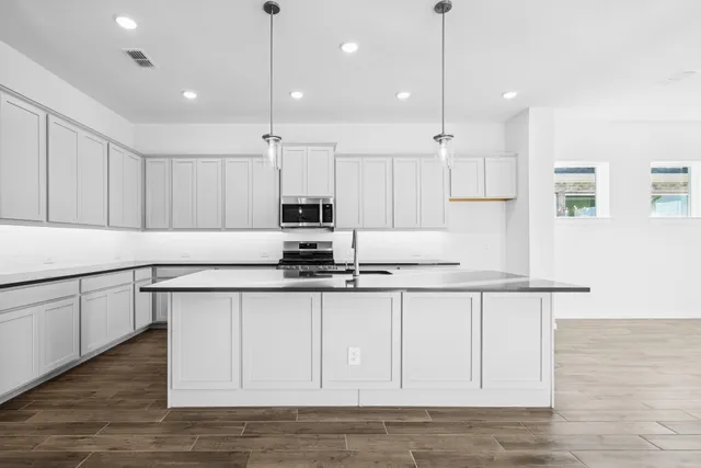 a kitchen with stainless steel appliances granite countertop a sink stove a refrigerator and white cabinets with wooden floor