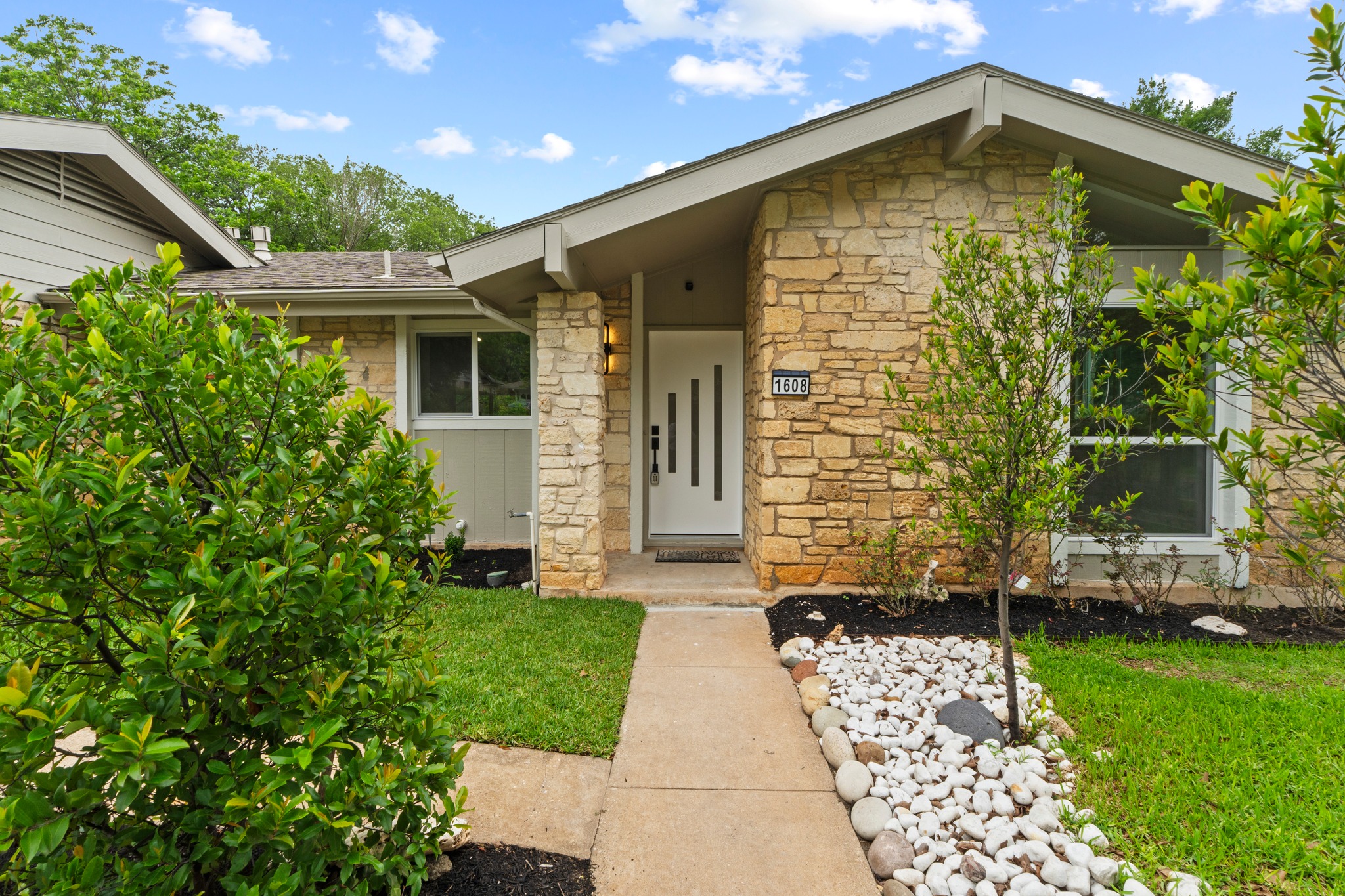 1608 Springer Lane Austin, TX 78758 - Photo 6 of 35 Stone facade exterior featuring a gabled roofline and a modern entry door with vertical accent panels
