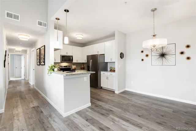 a kitchen with stainless steel appliances kitchen island a refrigerator a stove and white cabinets with wooden floor