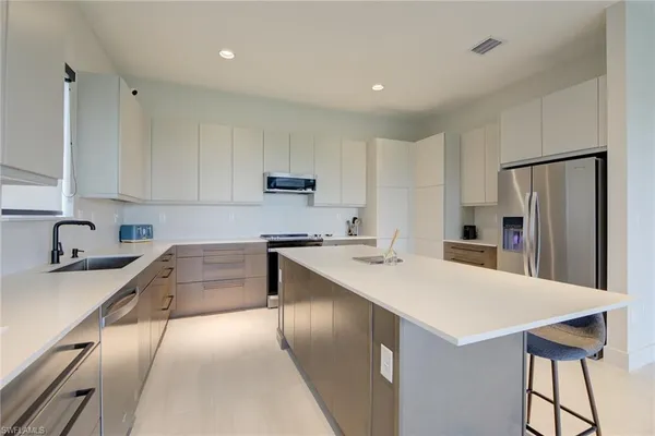 a kitchen with stainless steel appliances granite countertop a sink a stove a refrigerator and white cabinets with wooden floor