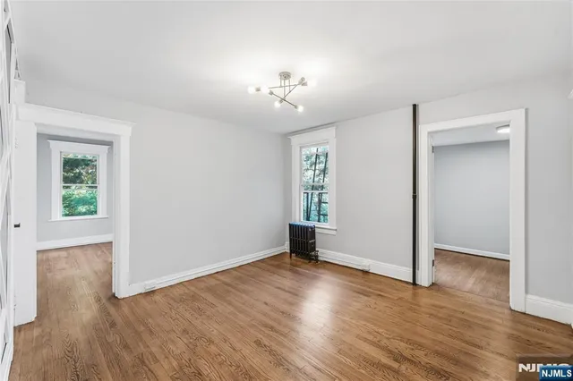 an empty room with wooden floor chandelier and windows