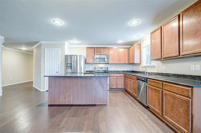 a kitchen with granite countertop wooden floors stainless steel appliances a sink and a window