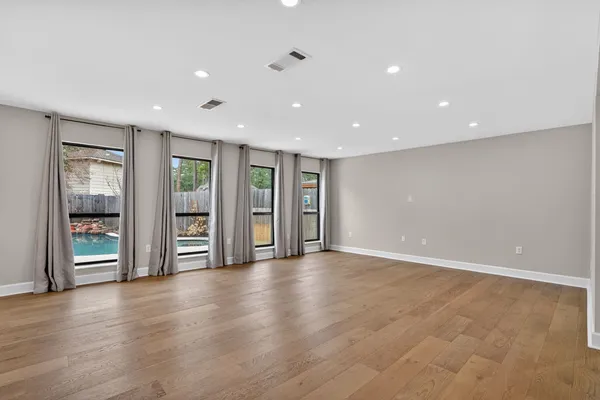 an empty room with wooden floor chandelier and windows