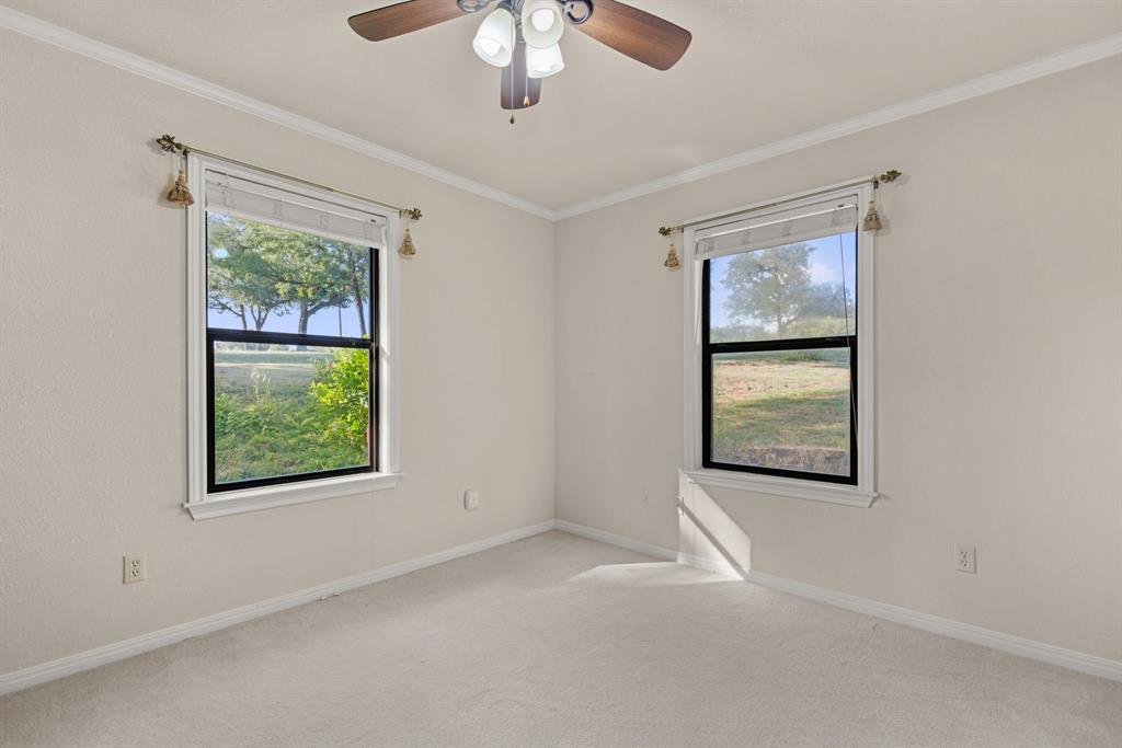 13539 Chapel Road Lorena, TX 76655 - Photo 24 of 37 Neutral tone walls with crown molding, two windows with black frames, and a ceiling fan with integrated lighting