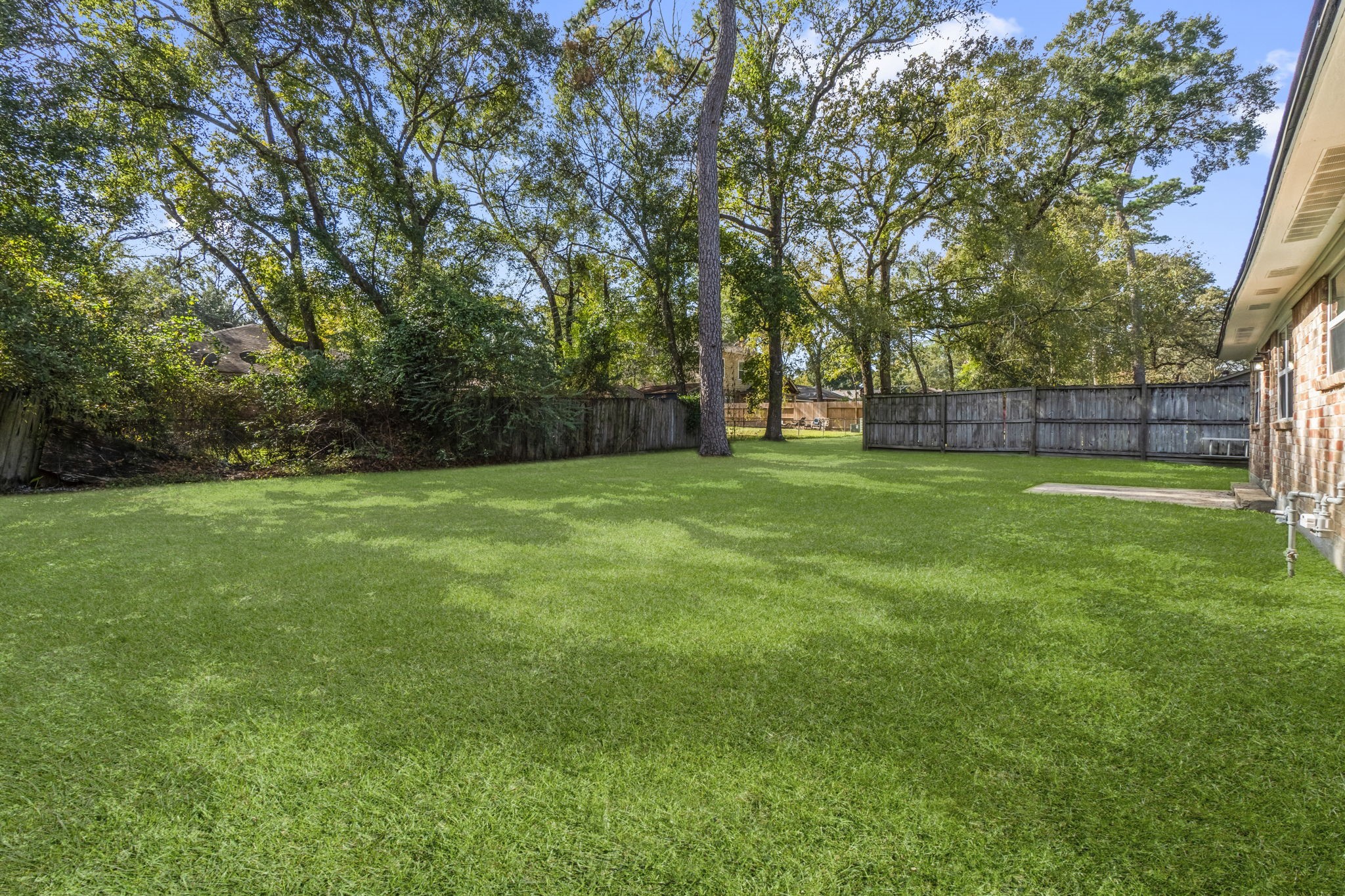 3223 Kentwood Drive Spring, TX 77380 - Photo 30 of 31 Spacious backyard featuring a large open lawn bordered by privacy fencing. A beautiful mature tree provides shade and character, creating the perfect setting for outdoor activities or future landscaping projects.