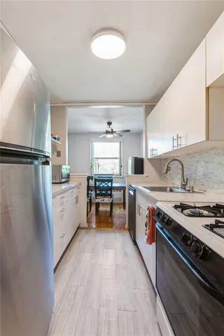 a kitchen with stainless steel appliances a stove a sink dishwasher a refrigerator white cabinets and wooden floor